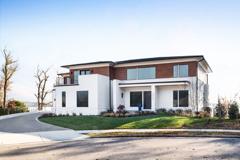 The exterior of this approximately 8,000 sq. ft. home is a combination of white stucco and black metal with brown, horizontal Trespa high-pressure laminate panels. 